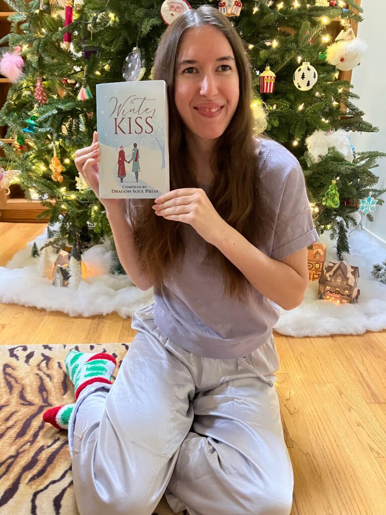 Demi smiling with her copy of A Winter Kiss by the Christmas tree