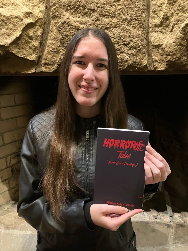 Demi smiling with her copy of HORRORific Tales Volume 1: Hauntings