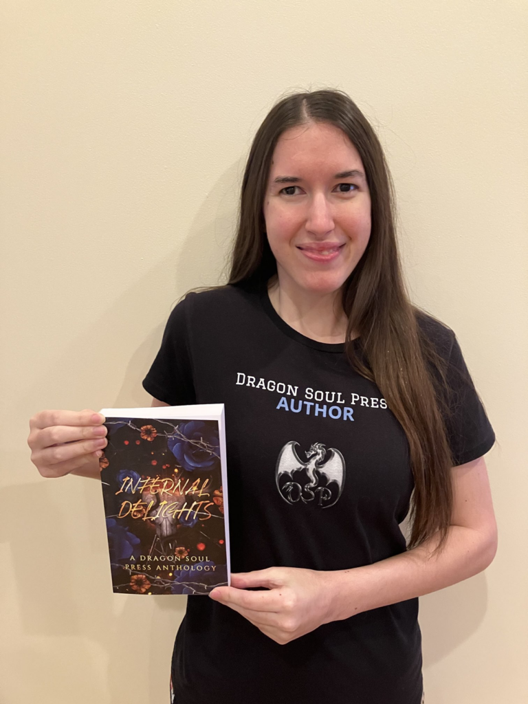 Demi smiling with her copy of Infernal Delights and wearing her Dragon Soul Press author shirt