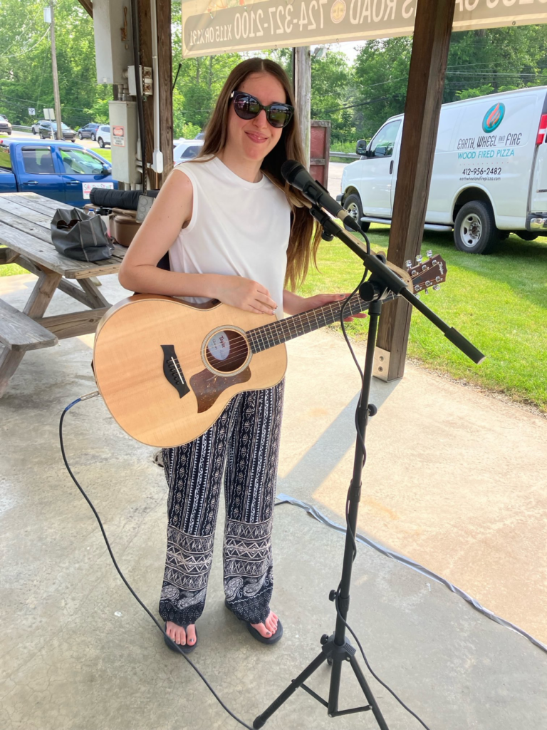 Demi smiling with her guitar by her microphone at the farmers market