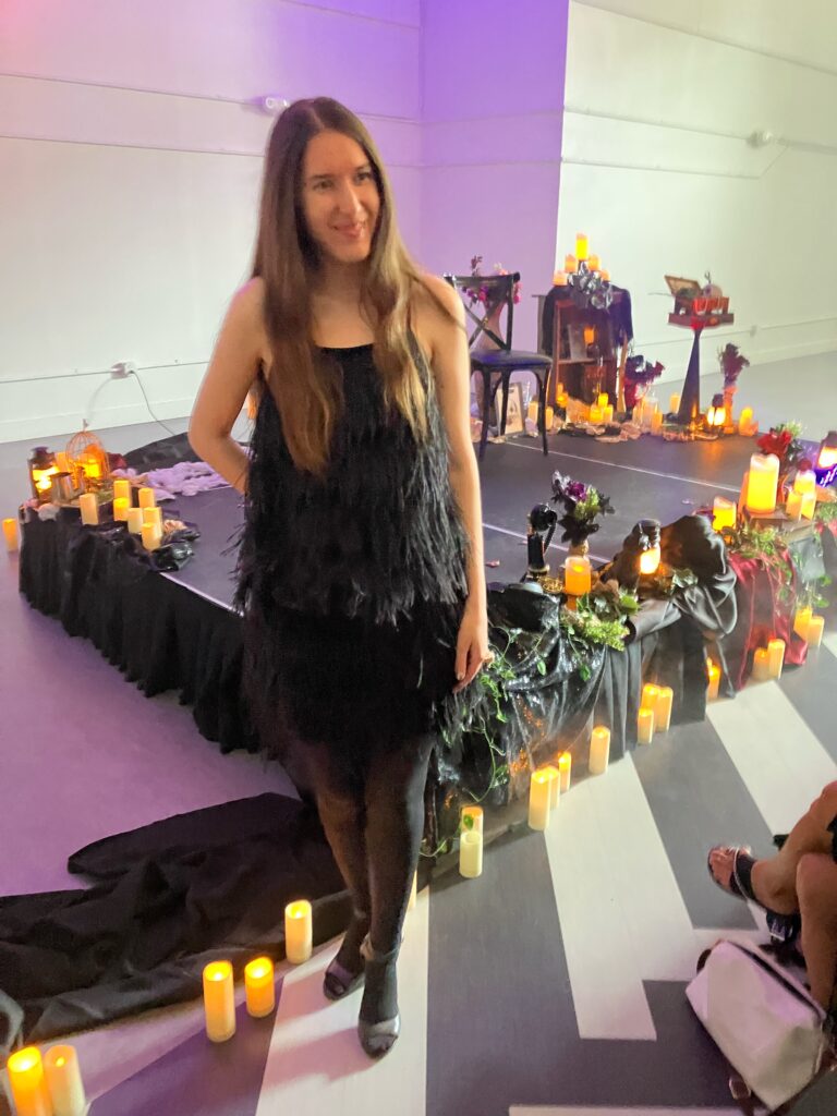 Demi at the Poe Speakeasy wearing a black feather top and skirt, black tights, and black boots