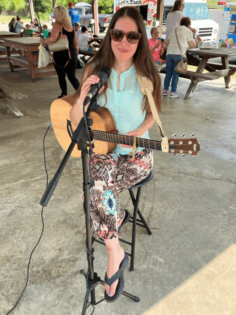 Demi Michelle with her guitar and microphone at the farmers market