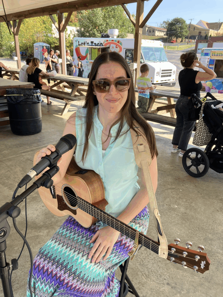 Demi Michelle smiling with her guitar and microphone at the farmers market